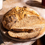 A round loaf of soda bread on a cutting board with two slices cut.