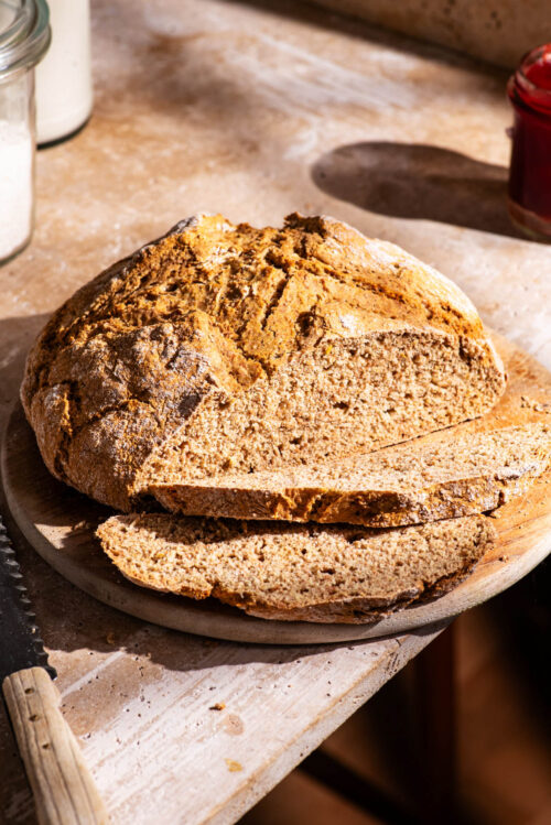 A round loaf of soda bread on a cutting board with two slices cut.