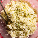 A glass cabbage-leaf bowl filled with cabbage salad on a gingham tablecloth.