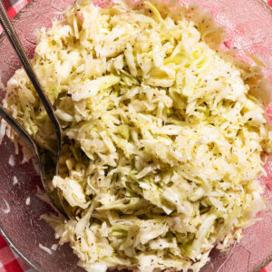 A glass cabbage-leaf bowl filled with cabbage salad on a gingham tablecloth.