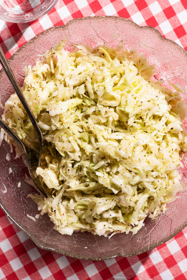 A glass cabbage-leaf bowl filled with cabbage salad on a gingham tablecloth.