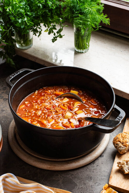 A large black pot filled with tomato vegetable soup in front of a windowsill.