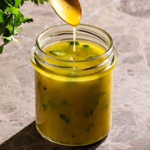 Salad dressing in a jar with a spoon drizzling the dressing.