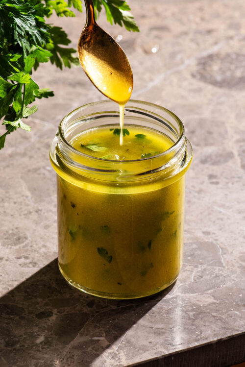 Salad dressing in a jar with a spoon drizzling the dressing.