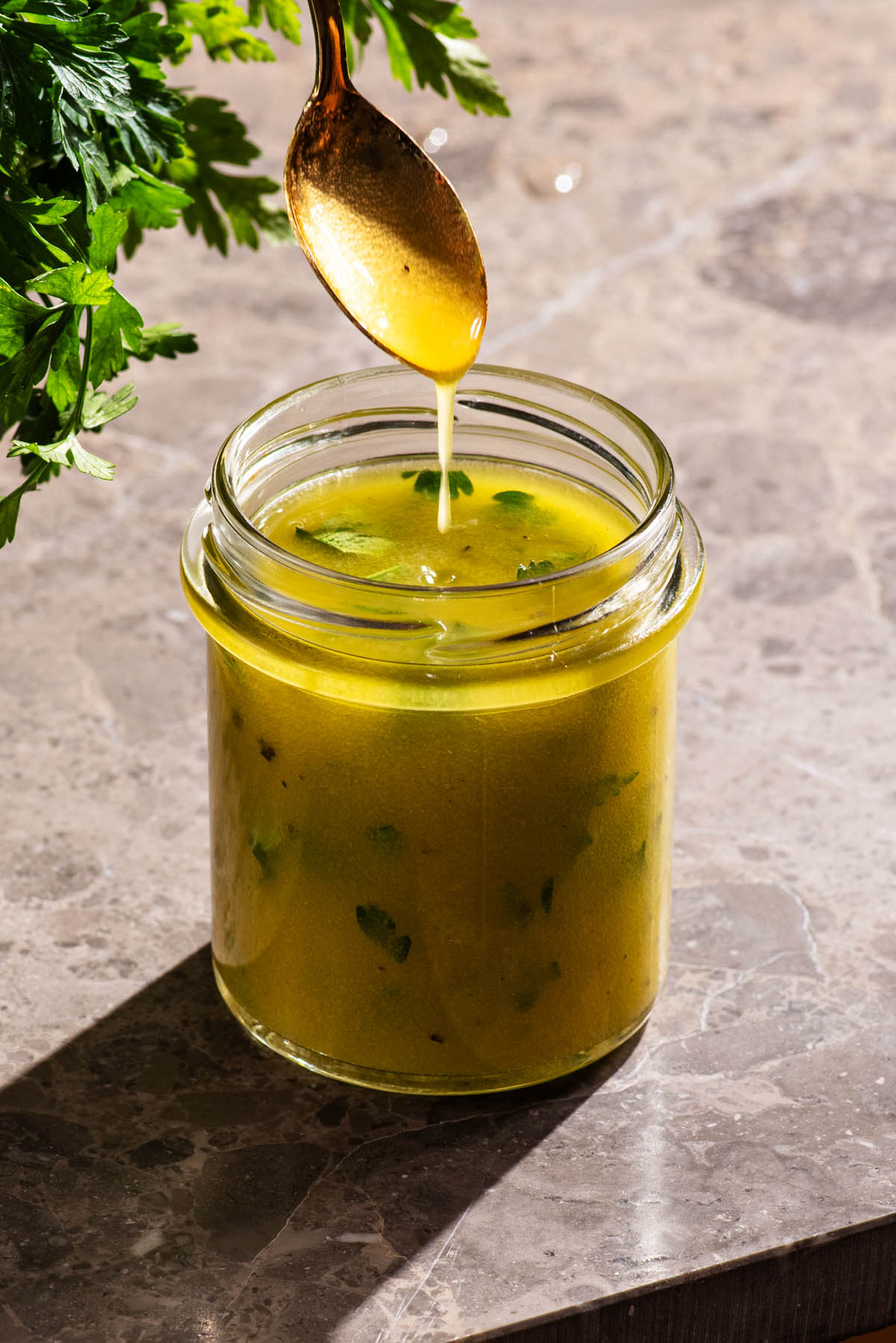 Salad dressing in a jar with a spoon drizzling the dressing.