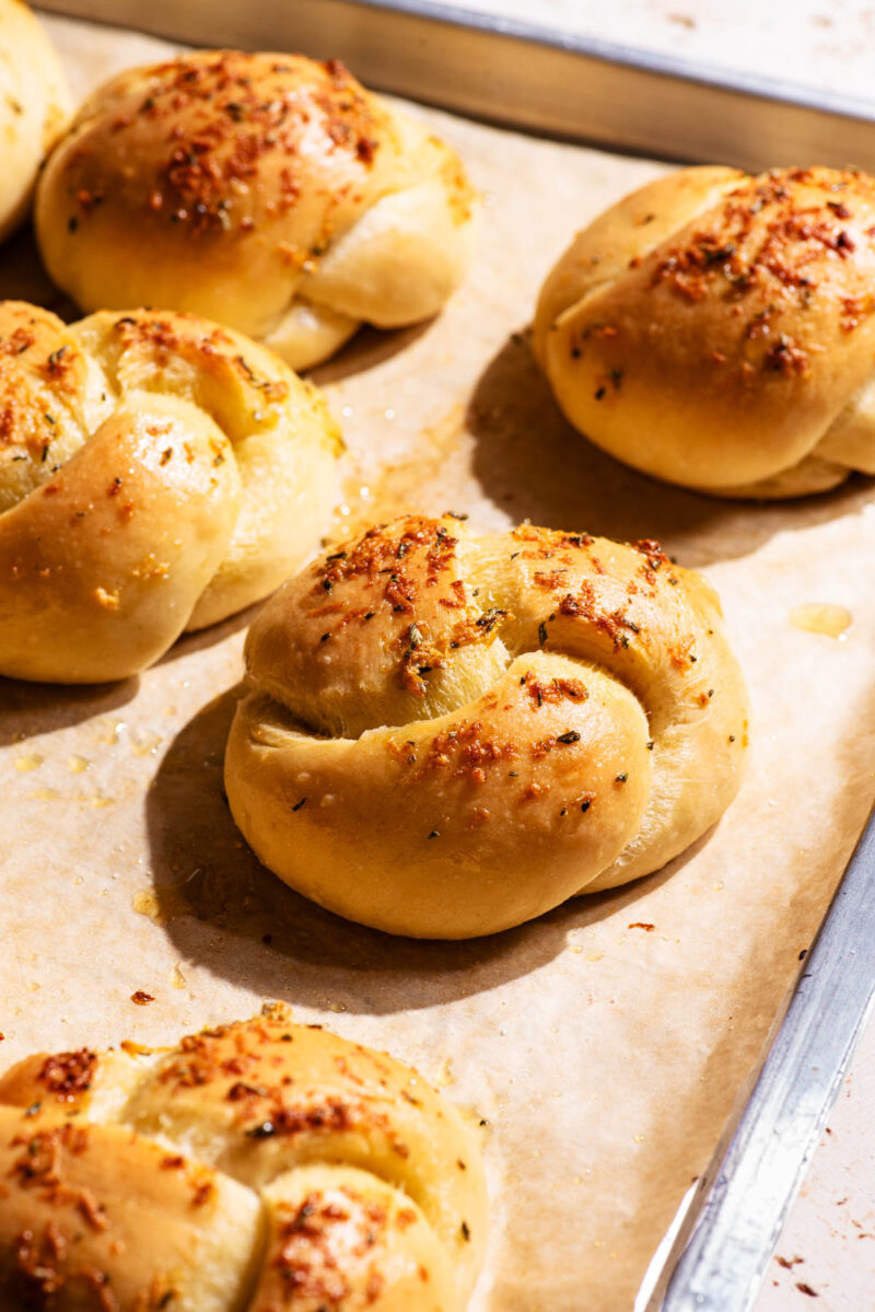 Twisted buns on a baking sheet, topped with baked garlic pieces.