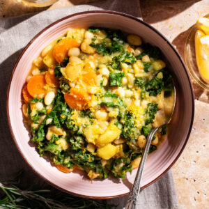 A bowl of bean and kale soup with a second bowl and drinks around.