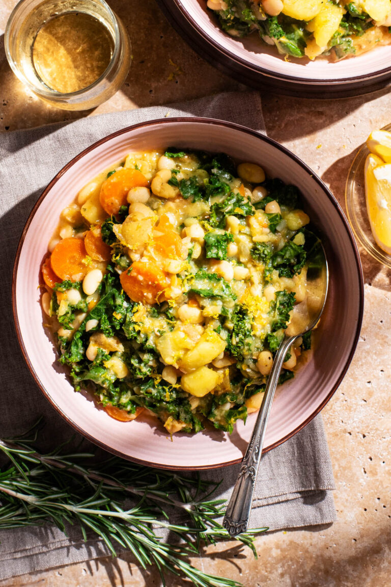 A bowl of bean and kale soup with a second bowl and drinks around.