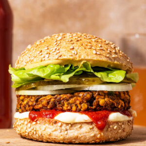 Vegetarian lentil burger on a bun with sauces and vegetable toppings.