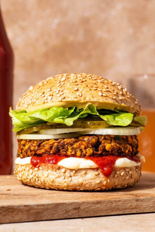 Vegetarian lentil burger on a bun with sauces and vegetable toppings.