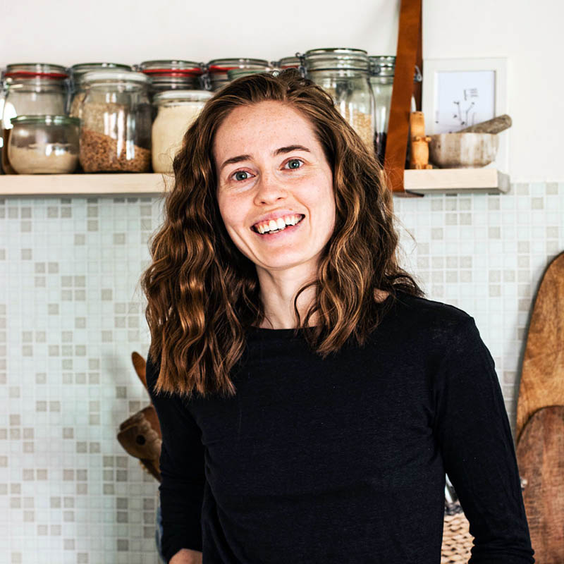 Woman smiling in a kitchen with open shelf at head height.