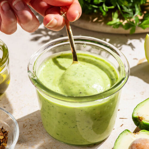 Smooth green dressing in a jar being stirred with a spoon.