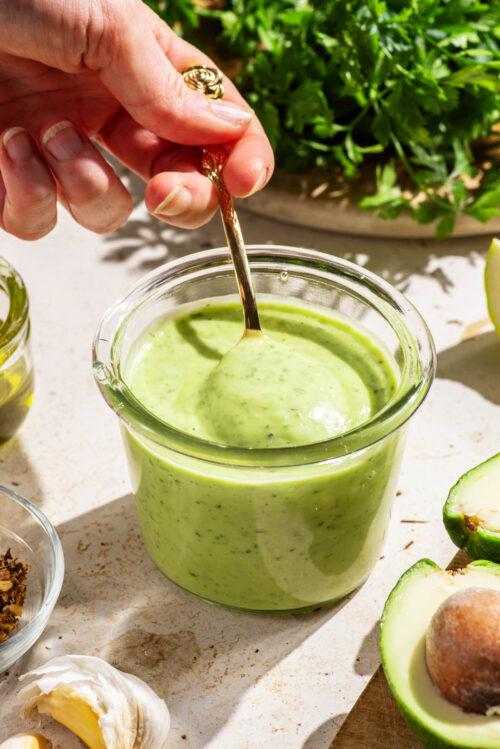 Smooth green dressing in a jar being stirred with a spoon.