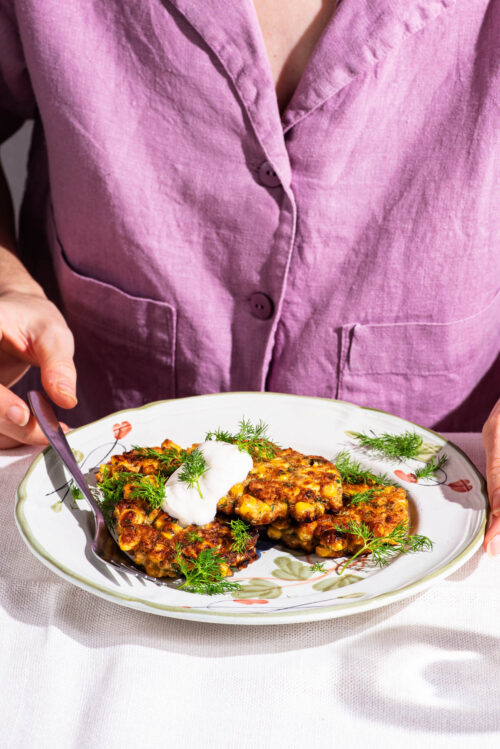 Woman sitting behind a plate with corn fritters.