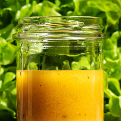Salad dressing in a glass jar in front of a head of green lettuce.