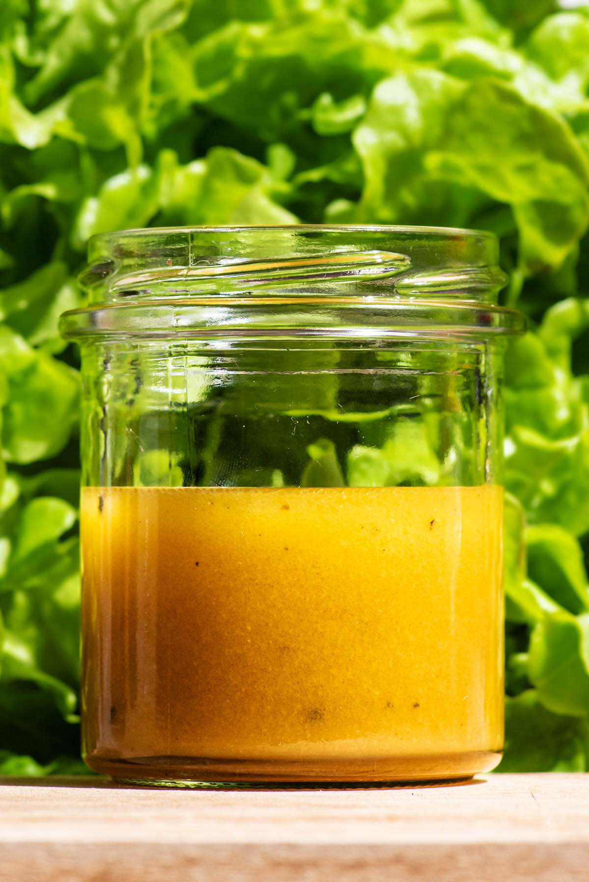 Salad dressing in a glass jar in front of a head of green lettuce.