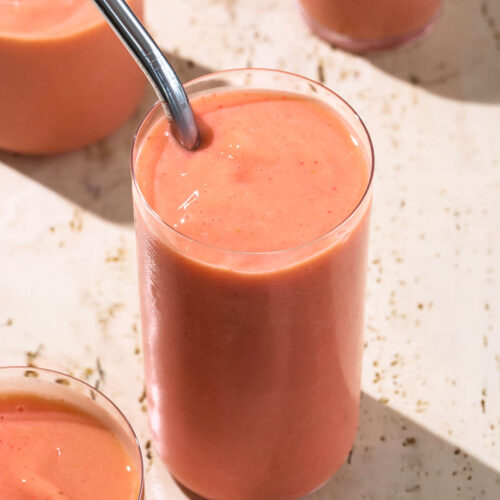 Pink-orange smoothie in four cups, one with a metal straw.