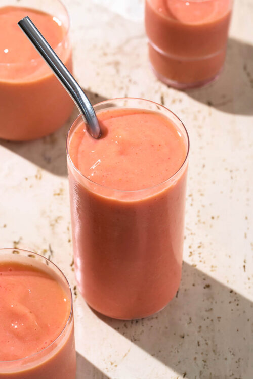 Pink-orange smoothie in four cups, one with a metal straw.