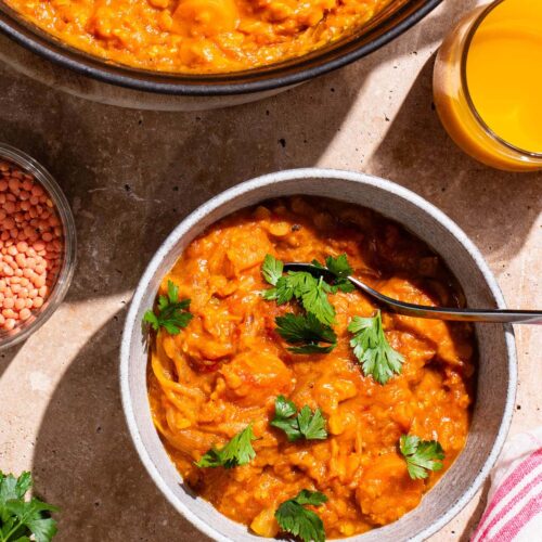 A bowl of orange curry with herbs on top, pot of curry beside.