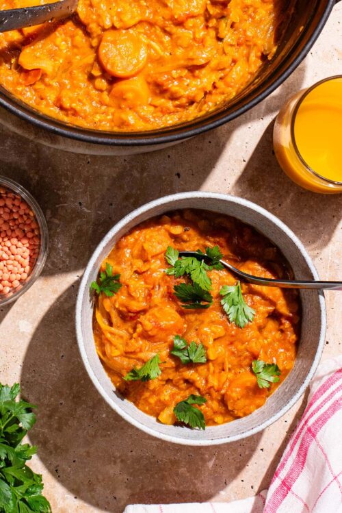 A bowl of orange curry with herbs on top, pot of curry beside.