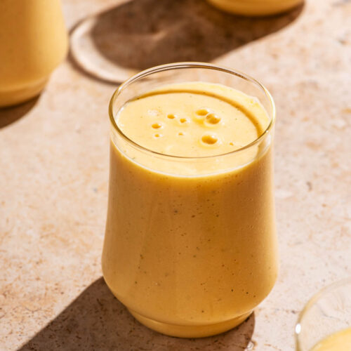 Light orange smoothie in glasses on a stone background.