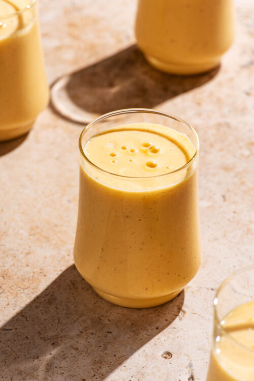Light orange smoothie in glasses on a stone background.