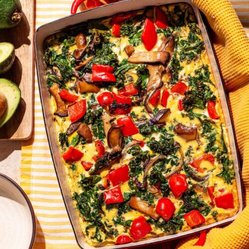 A vegetable frittata in a rectangular baking dish with avocado beside.