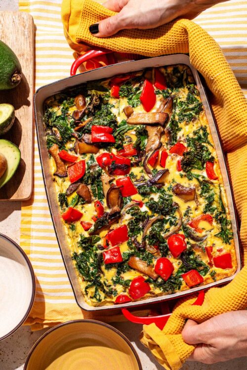 A vegetable frittata in a rectangular baking dish with avocado beside.
