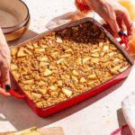 Woman's hands placing red baking dish with baked oatmeal on a table.