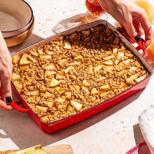 Woman's hands placing red baking dish with baked oatmeal on a table.