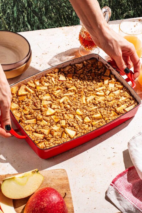 Woman's hands placing red baking dish with baked oatmeal on a table.