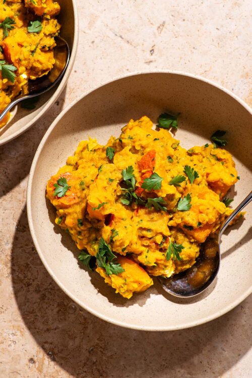 Two bowls with a thick lentil curry topped with parsley.