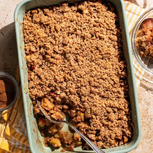 A rectangular baking dish of apple crumble with a spoonful taken out.