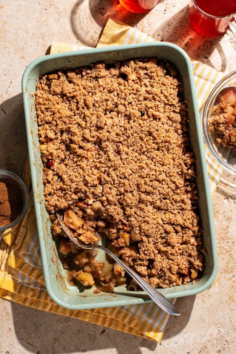 A rectangular baking dish of apple crumble with a spoonful taken out.