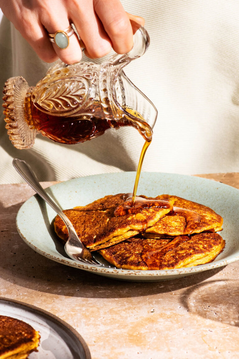 Pouring maple syrup over a plate of three orange pancakes on a green plate.