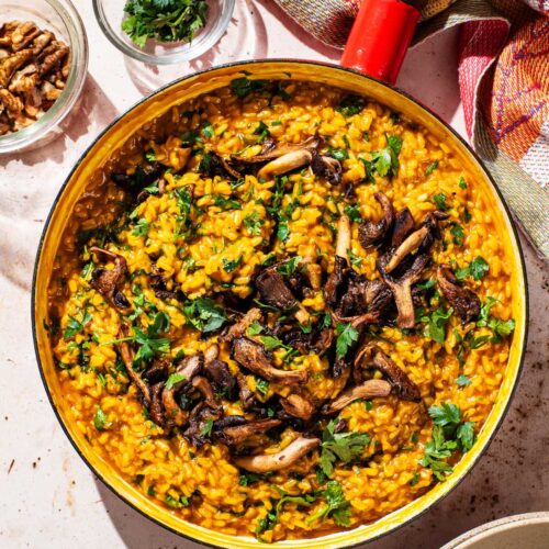 A large pan filled with orange risotto and topped with mushrooms and parsley.