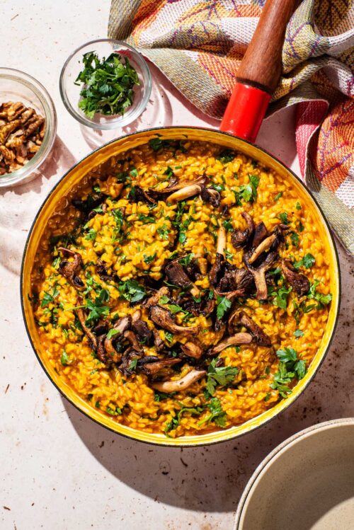 A large pan filled with orange risotto and topped with mushrooms and parsley.
