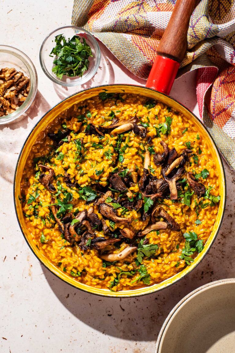 A large pan filled with orange risotto and topped with mushrooms and parsley.