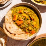Two bowls of curry with flatbread and a pot in the corner.
