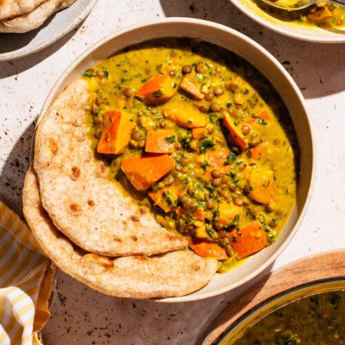 Two bowls of curry with flatbread and a pot in the corner.