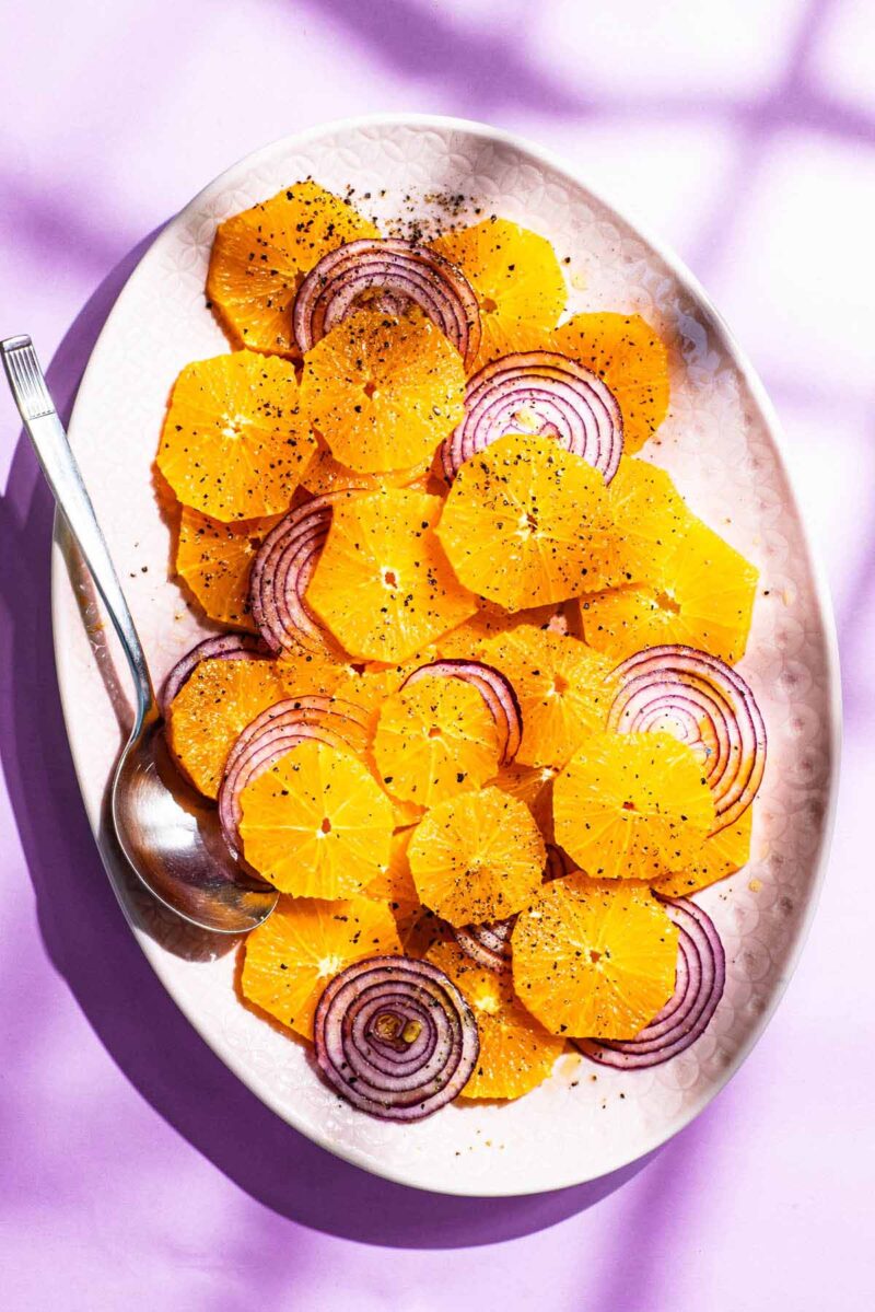 A platter of thinly sliced oranges and red onions with black pepper.