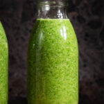 Green smoothie in small glass bottles on a small wooden board.