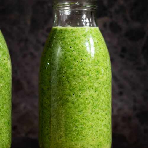 Green smoothie in small glass bottles on a small wooden board.