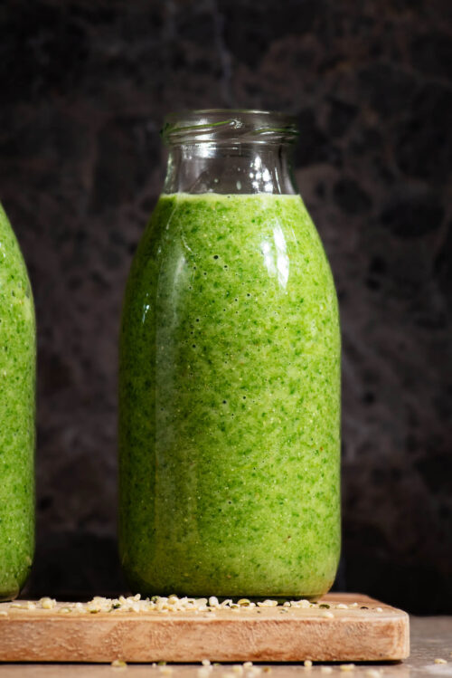 Green smoothie in small glass bottles on a small wooden board.