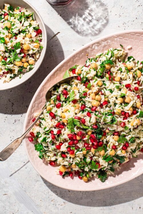 Pink serving platter with rice, parsley, and pomegranate salad.