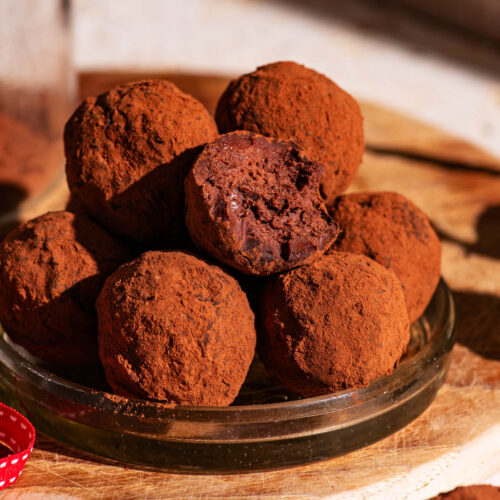 Several cocoa-coated truffles piled together, one with a bite taken out.