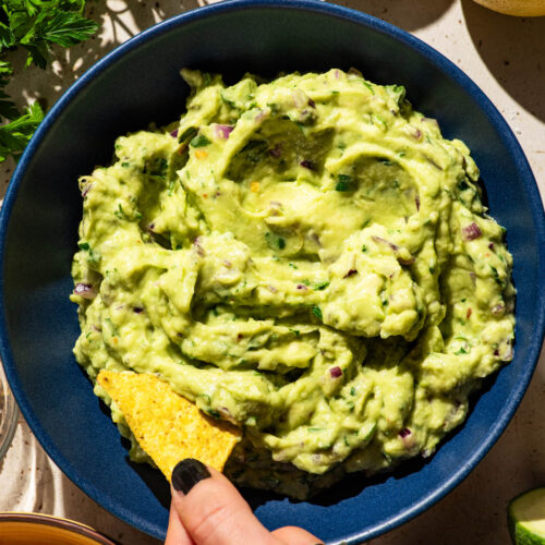 Guacamole in a blue bowl with a chip being dipped into it.