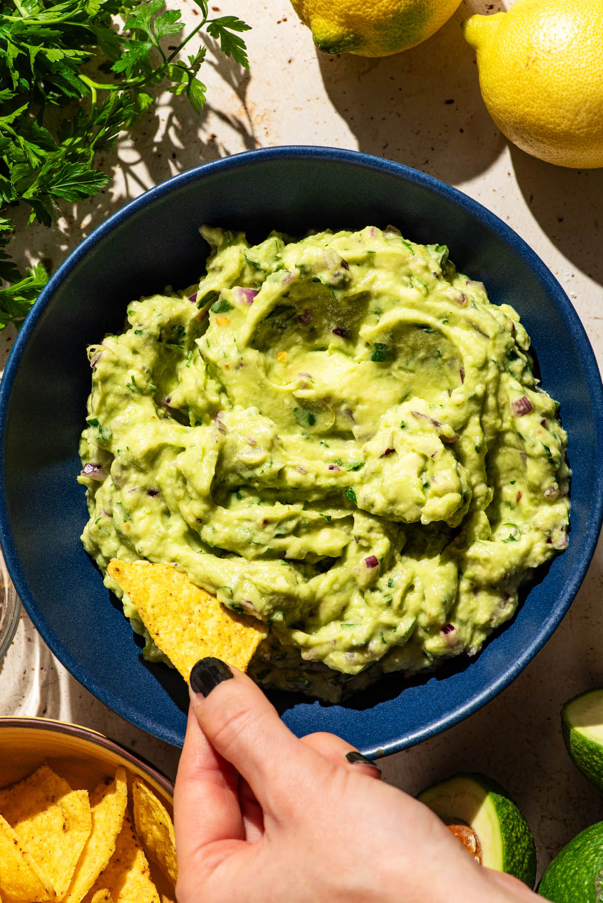 Guacamole in a blue bowl with a chip being dipped into it.