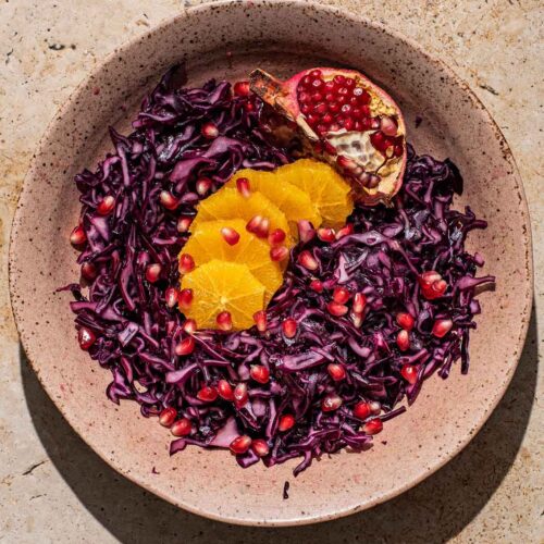 A shallow bowl of red cabbage salad with orange and pomegranate.