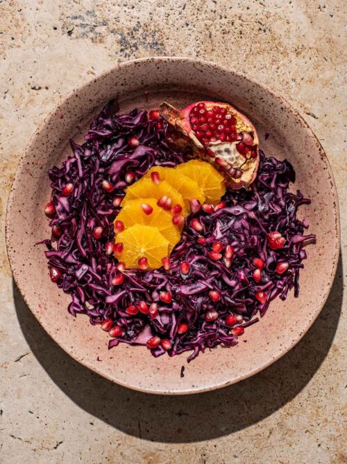 A shallow bowl of red cabbage salad with orange and pomegranate.